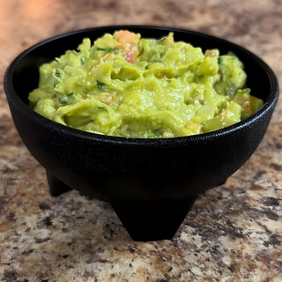 Fresh guacamole with visible chunks of avocado and tomato in a black molcajete bowl.