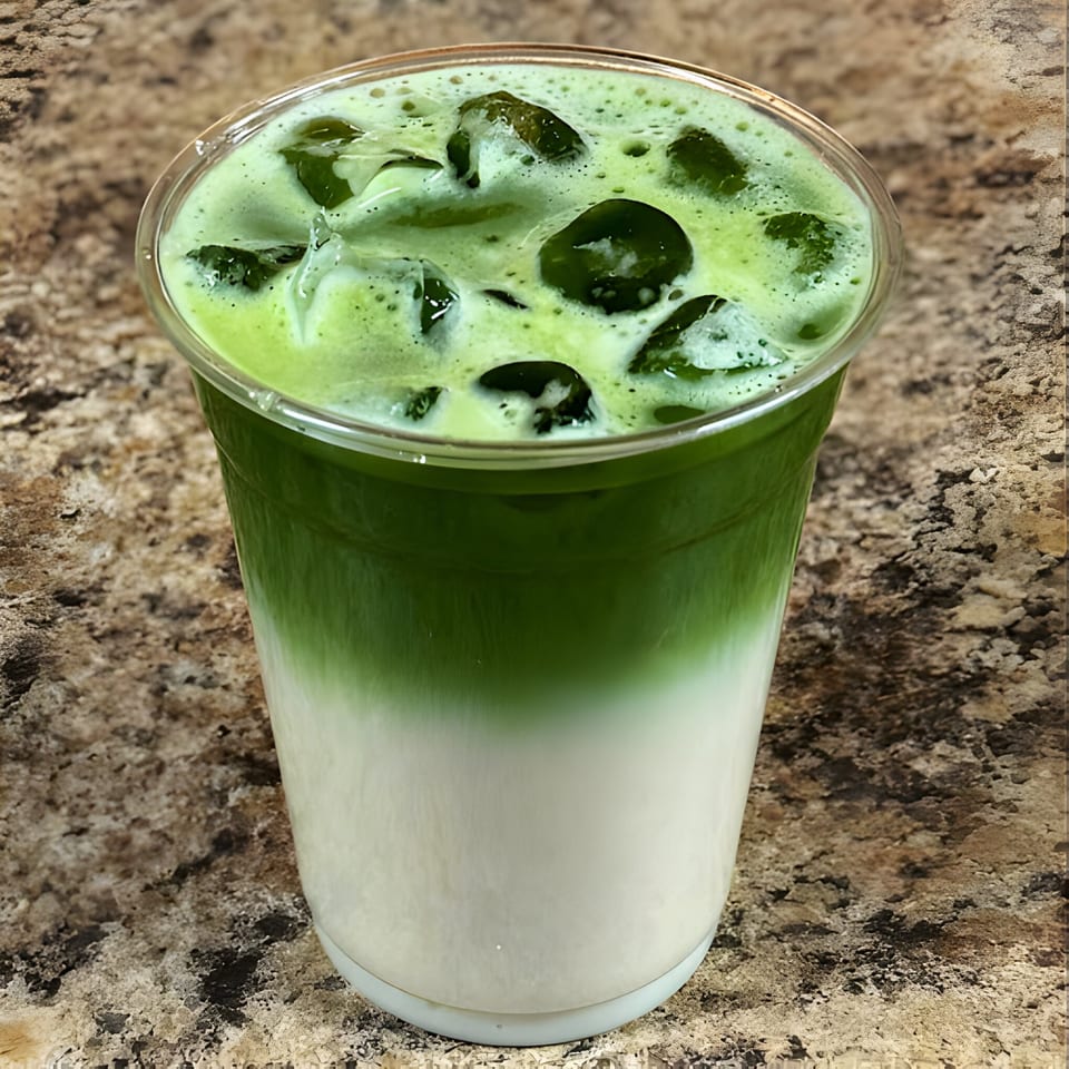Iced matcha latte with green tea and milk layers, topped with ice, on a textured brown surface.