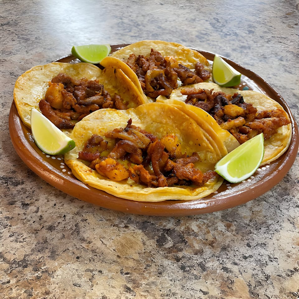 Four La Carreta Mexican tacos with meat and lime wedges on a brown plate.